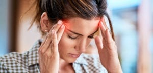 Woman with headache pushing fingers into temples, sign of possible TMJ disorder
