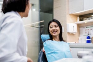 young woman sitting in dental chair smiling with dental specialist nearby
