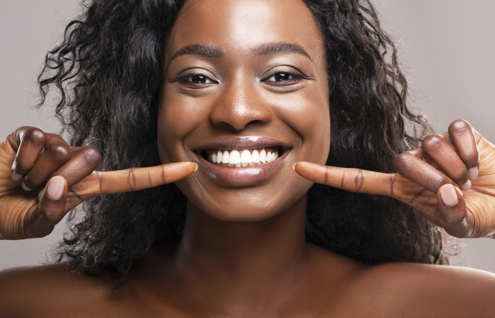 Happy african american girl pointing at her wide smile with two forefingers over grey background, closeup