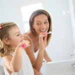 Mother and daughter in bathroom brushing her teeth