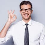 Happy young man in shirt and tie gesturing OK sign and smiling