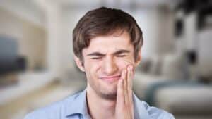 A man with peri-implantitis holding his jaw
