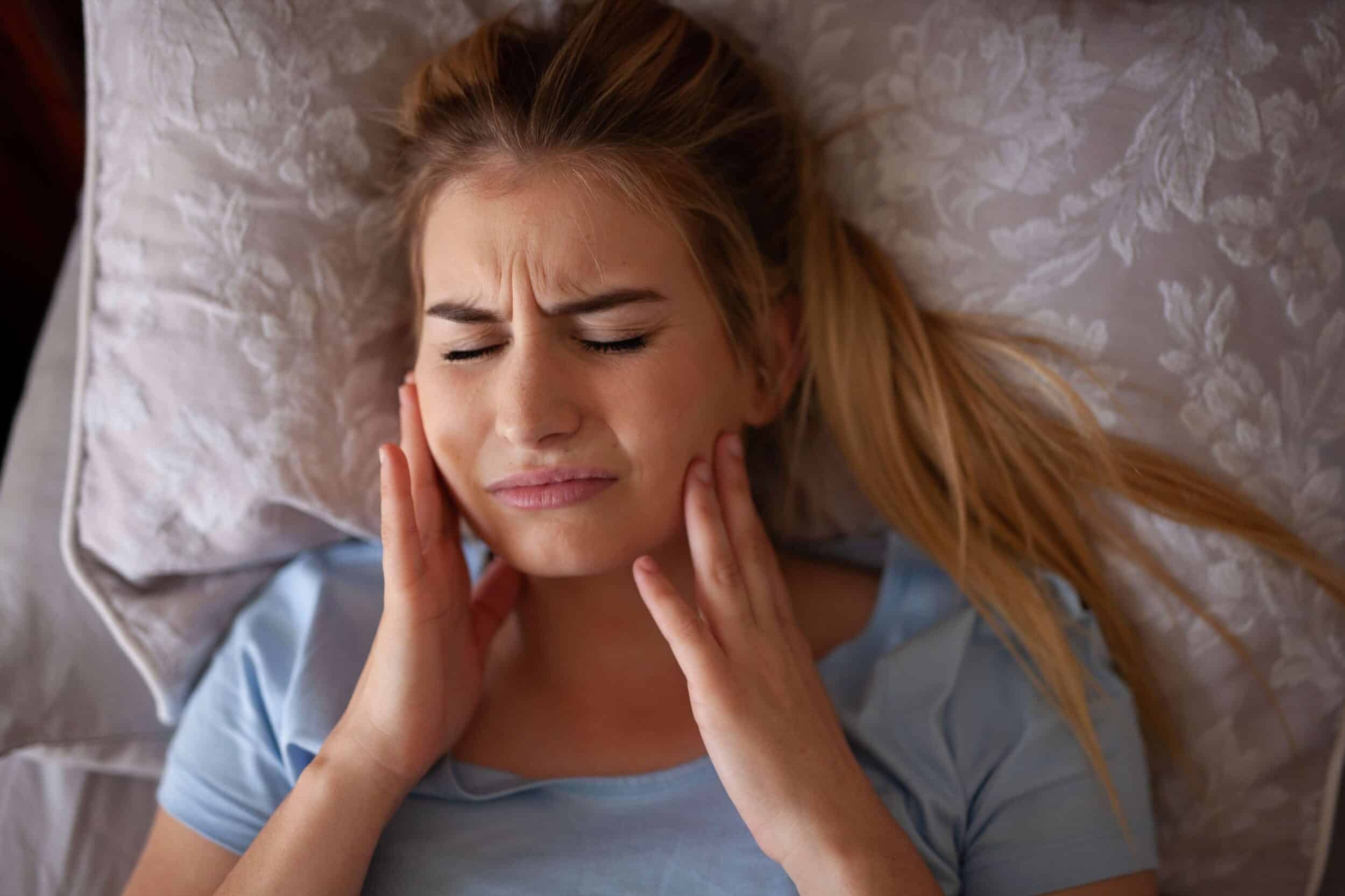 A woman with a TMJ disorder lying in bed and holding her jaw